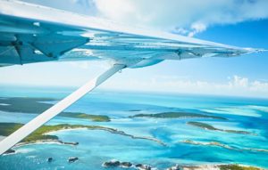 A plane wing soaring above the stunning blue ocean en route to Staniel Cay in the Bahamas.
