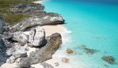 Fly to the Bahamas with Makers Air and experience an aerial view of Staniel Cay's stunning beach with turquoise water and rocky cliffs.