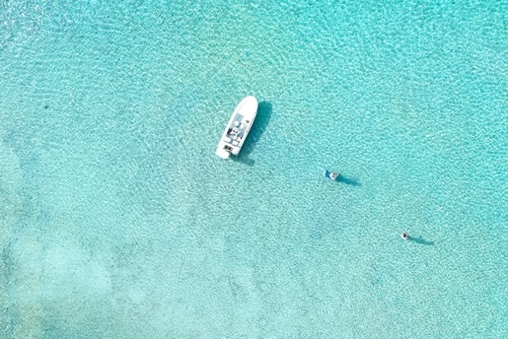Aerial view of a boat and two swimmers in clear turquoise water.