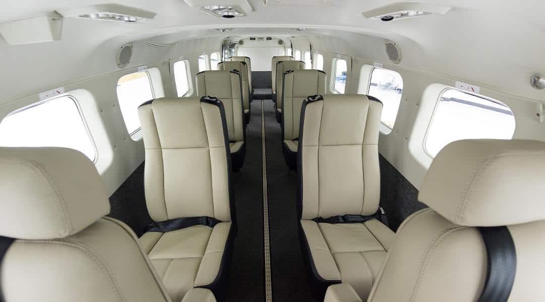 Interior view of a small airplane with beige leather seats and multiple windows on both sides.