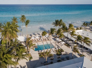 Aerial view of a beach resort with palm trees, pool, and ocean.