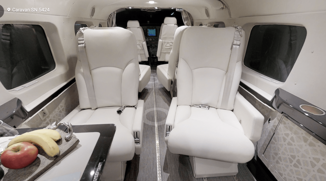 Luxurious aircraft interior with white seats and fruit on a table.