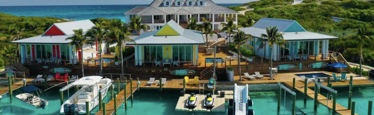 a-boat-docked-in-the-water-next-to-a-colorful-house-on-staniel-cay-768×236