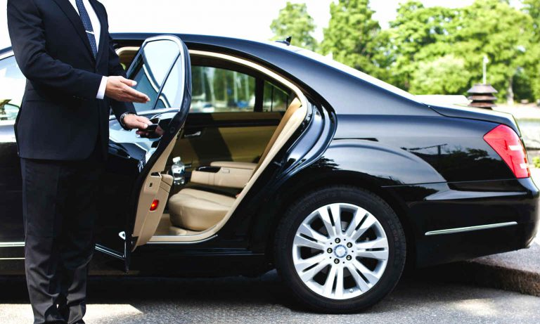 Man in suit opening black luxury car door with beige interior.