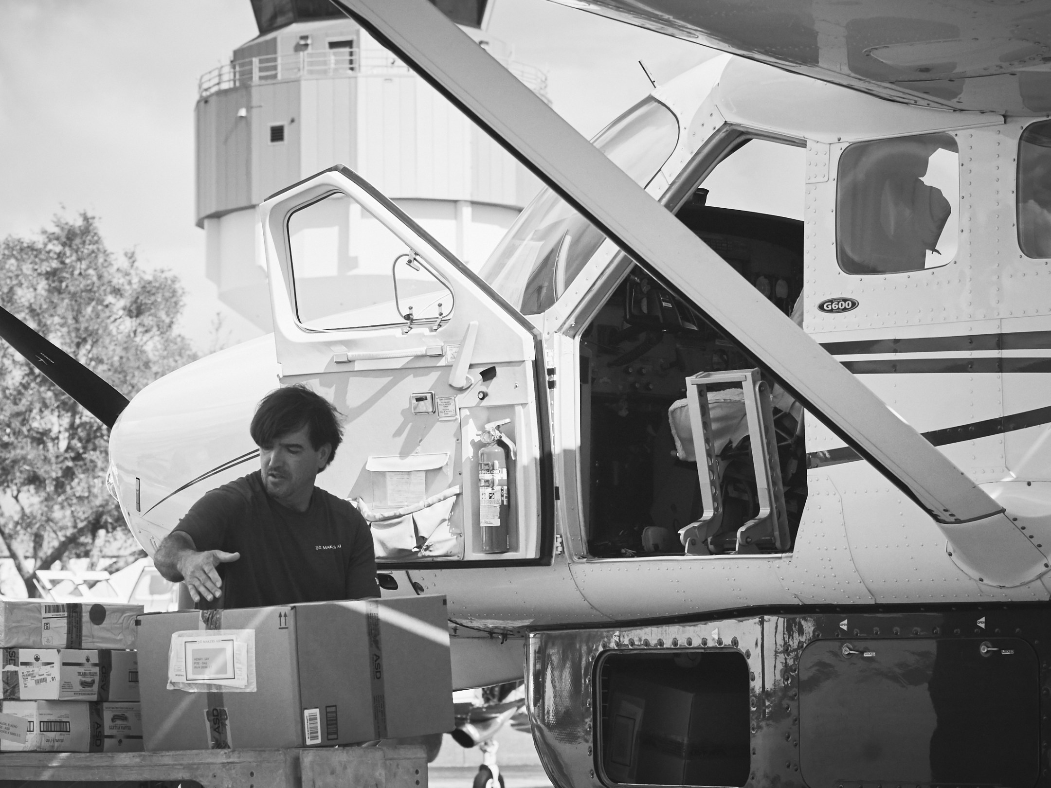 Person loading boxes onto a small airplane parked outdoors.