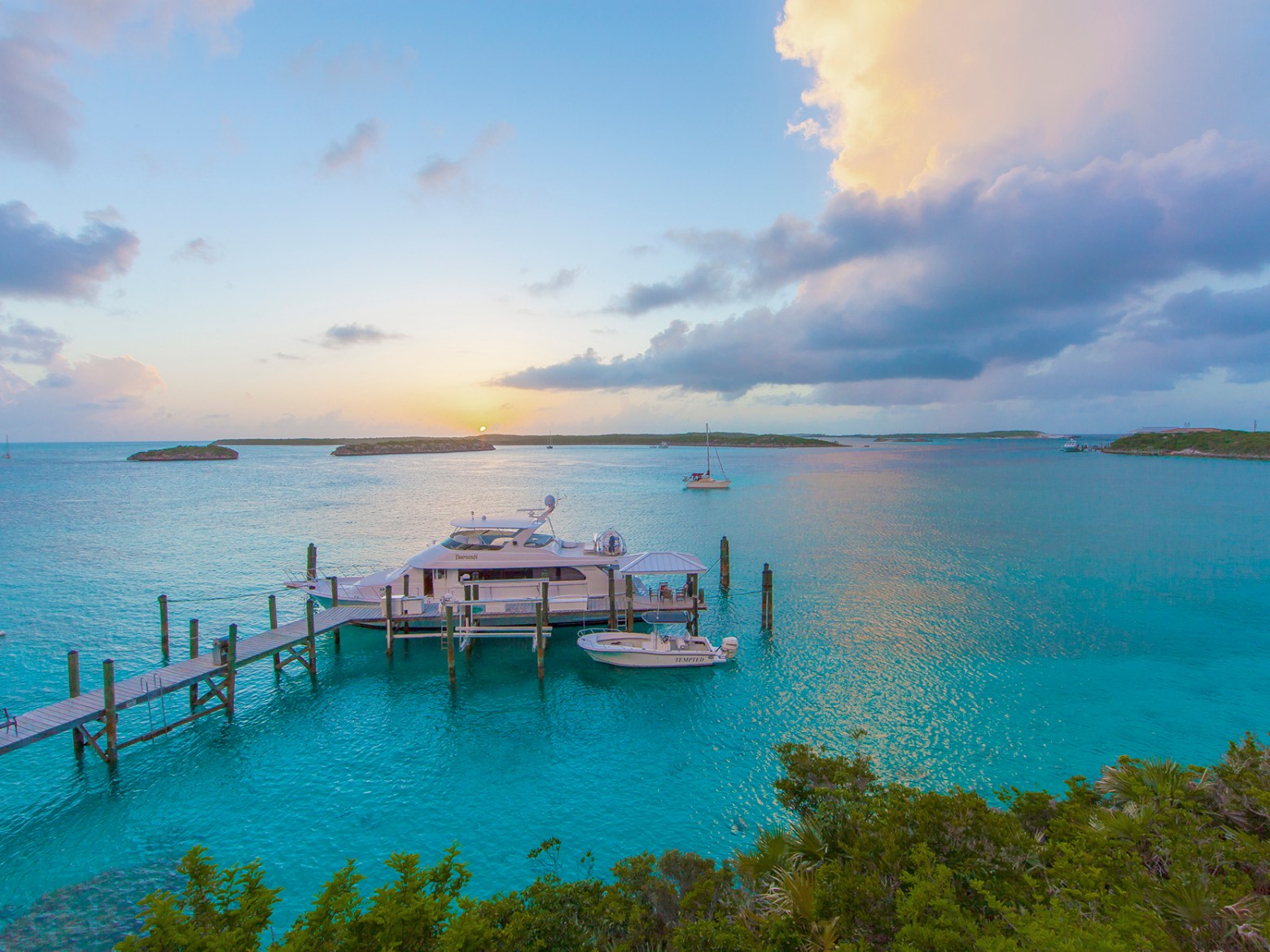 Scenic view of a dock with boats on turquoise water under a colorful sunset sky.
