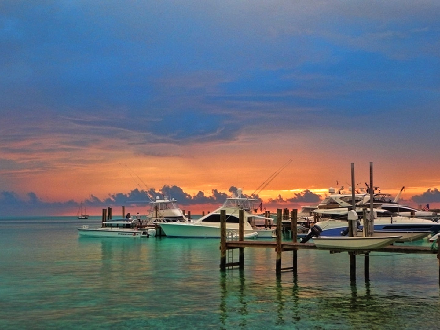 Boats at a dock with a colorful sunset over a calm sea and cloudy sky.