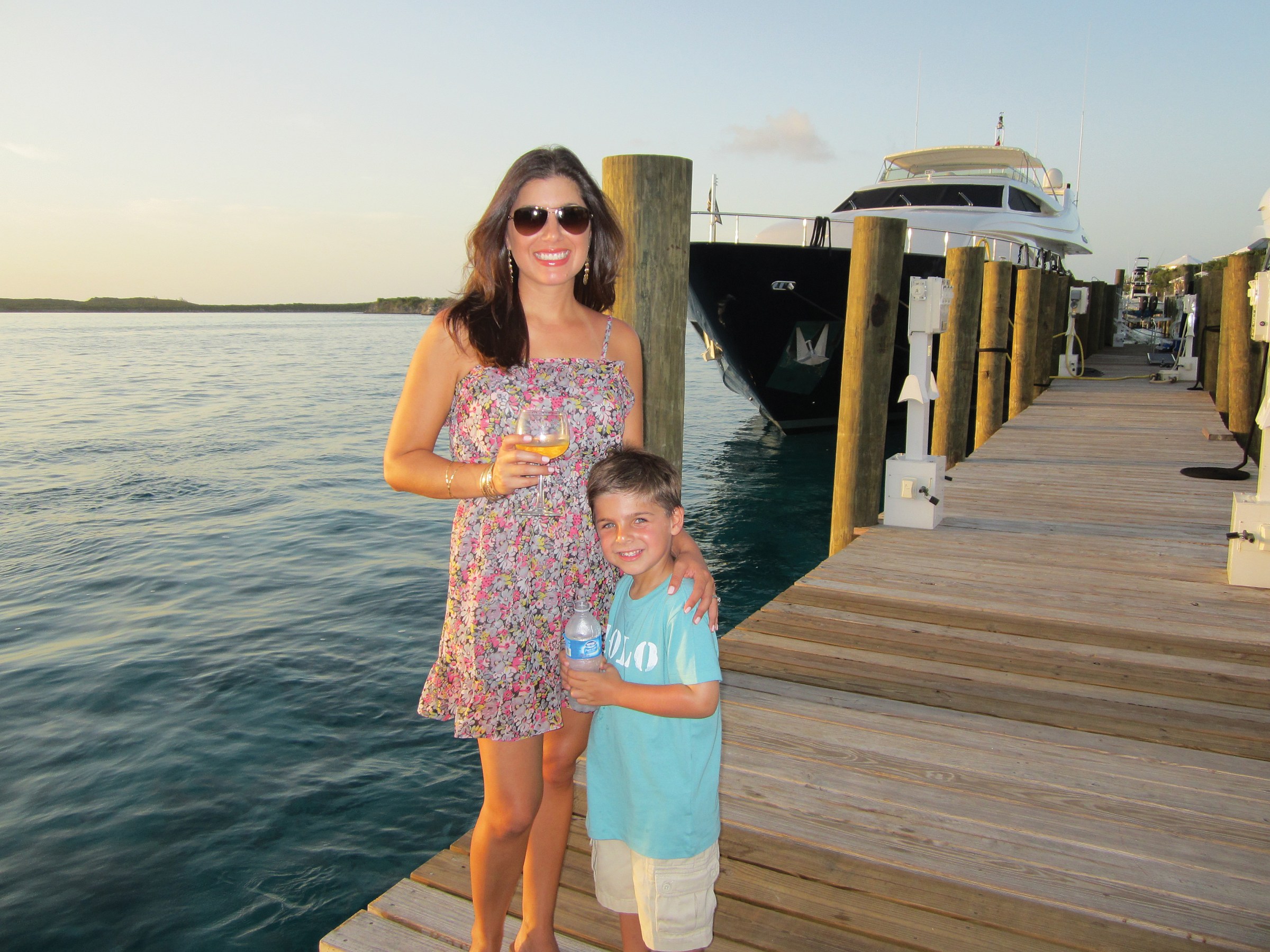 Woman and boy standing on a dock with a yacht in the background.