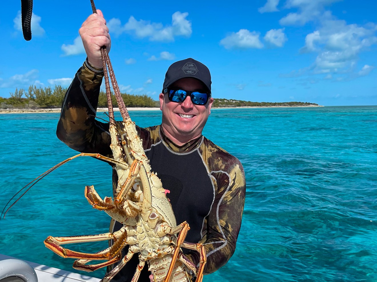 Person on a boat holding a large lobster with turquoise sea and blue sky background.