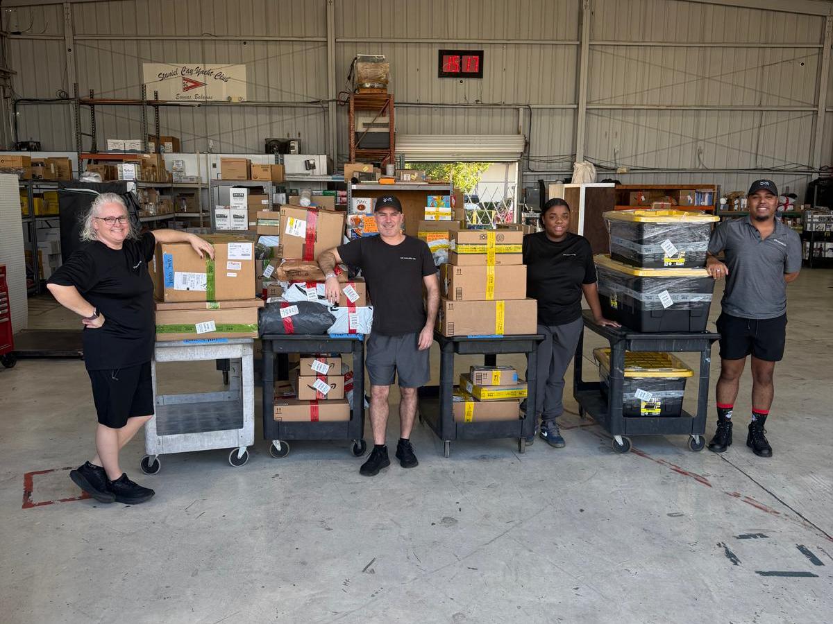 Four people in a warehouse standing by carts filled with packages.