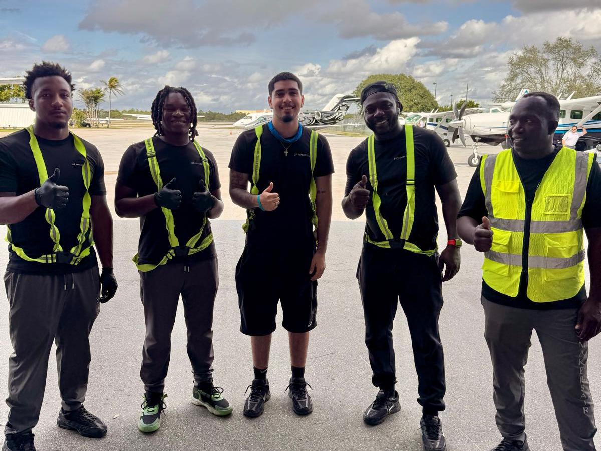 Five people wearing safety vests giving thumbs up on an airfield.