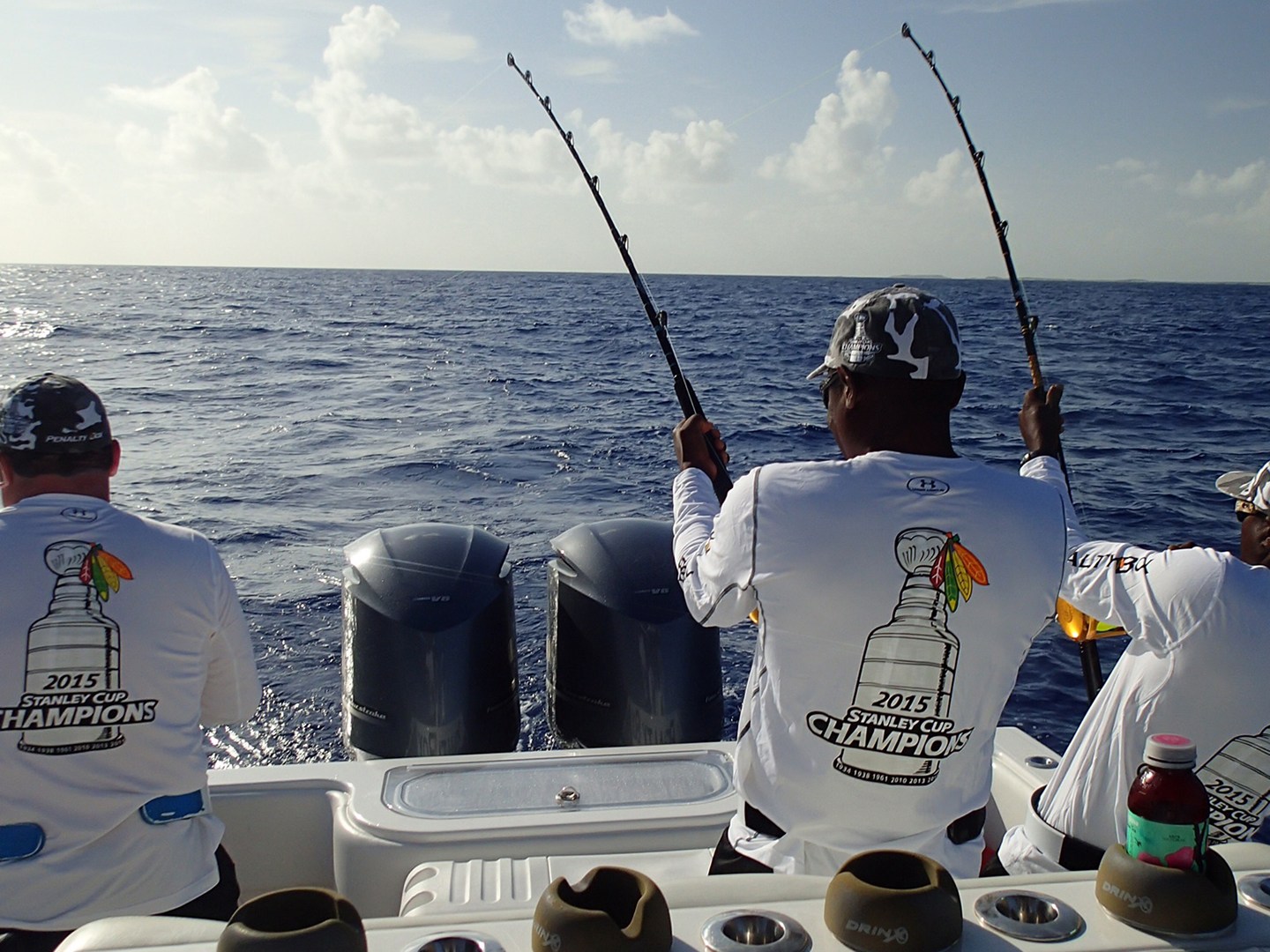 Three people fishing on a boat wearing matching shirts with championship logos.