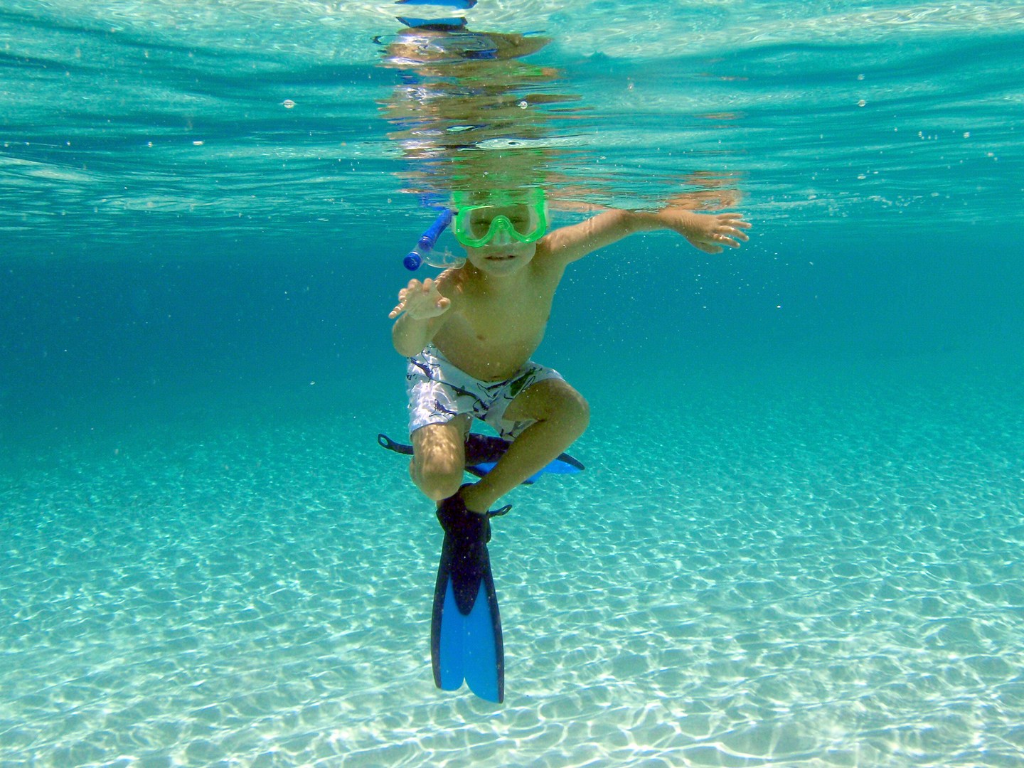 Child snorkeling underwater with mask, snorkel, and flippers in clear blue water.