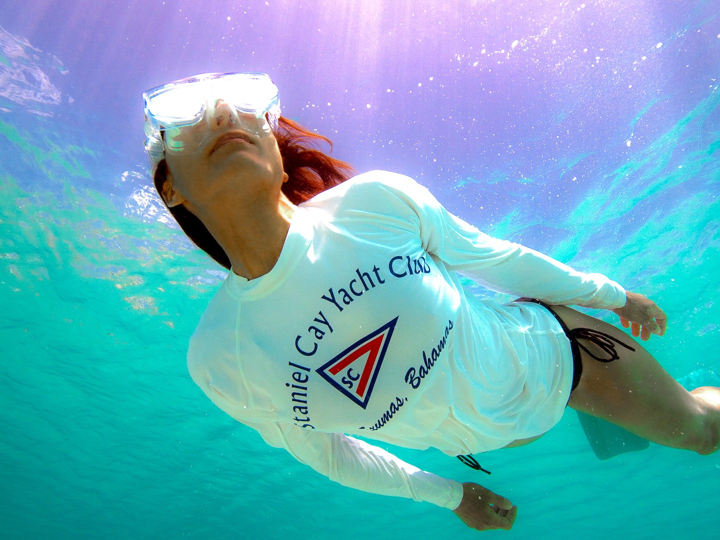 Person in white shirt snorkeling underwater in turquoise sea.