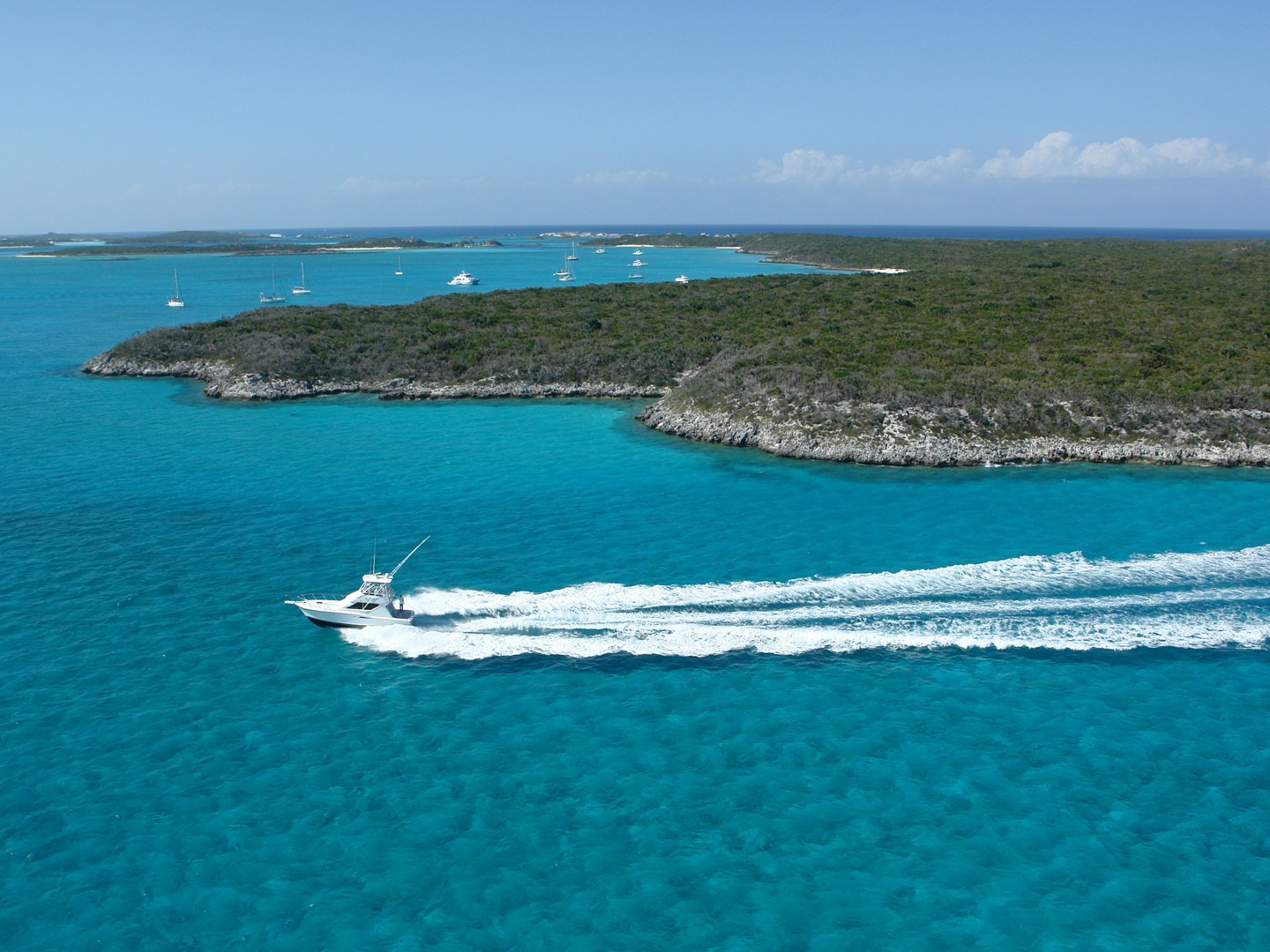 A boat speeds across clear turquoise water near islands under a blue sky.