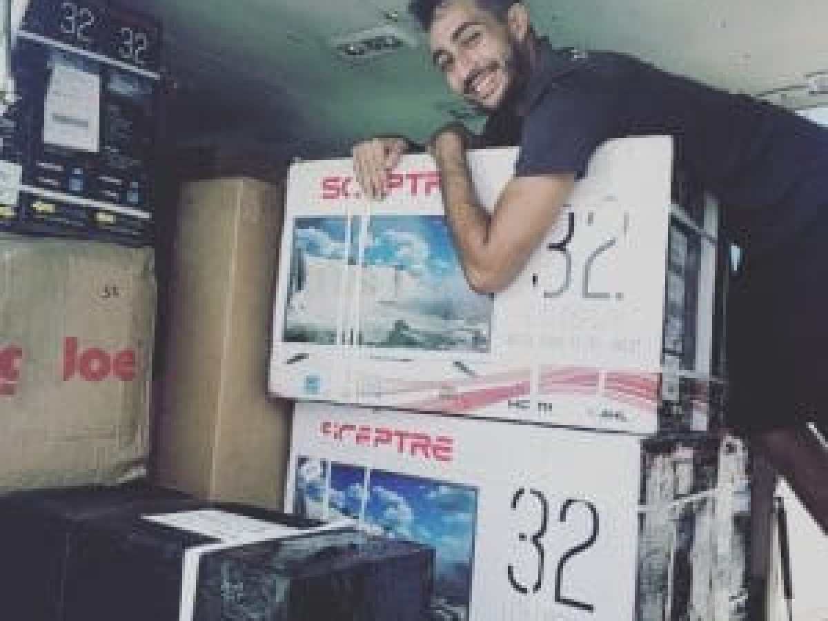 Man smiling and hugging boxed Sceptre TVs in a delivery van.