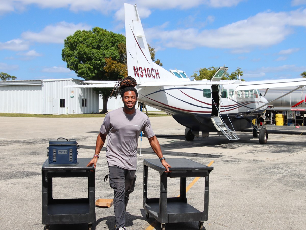 Person with carts smiling near a small aircraft on a sunny day.