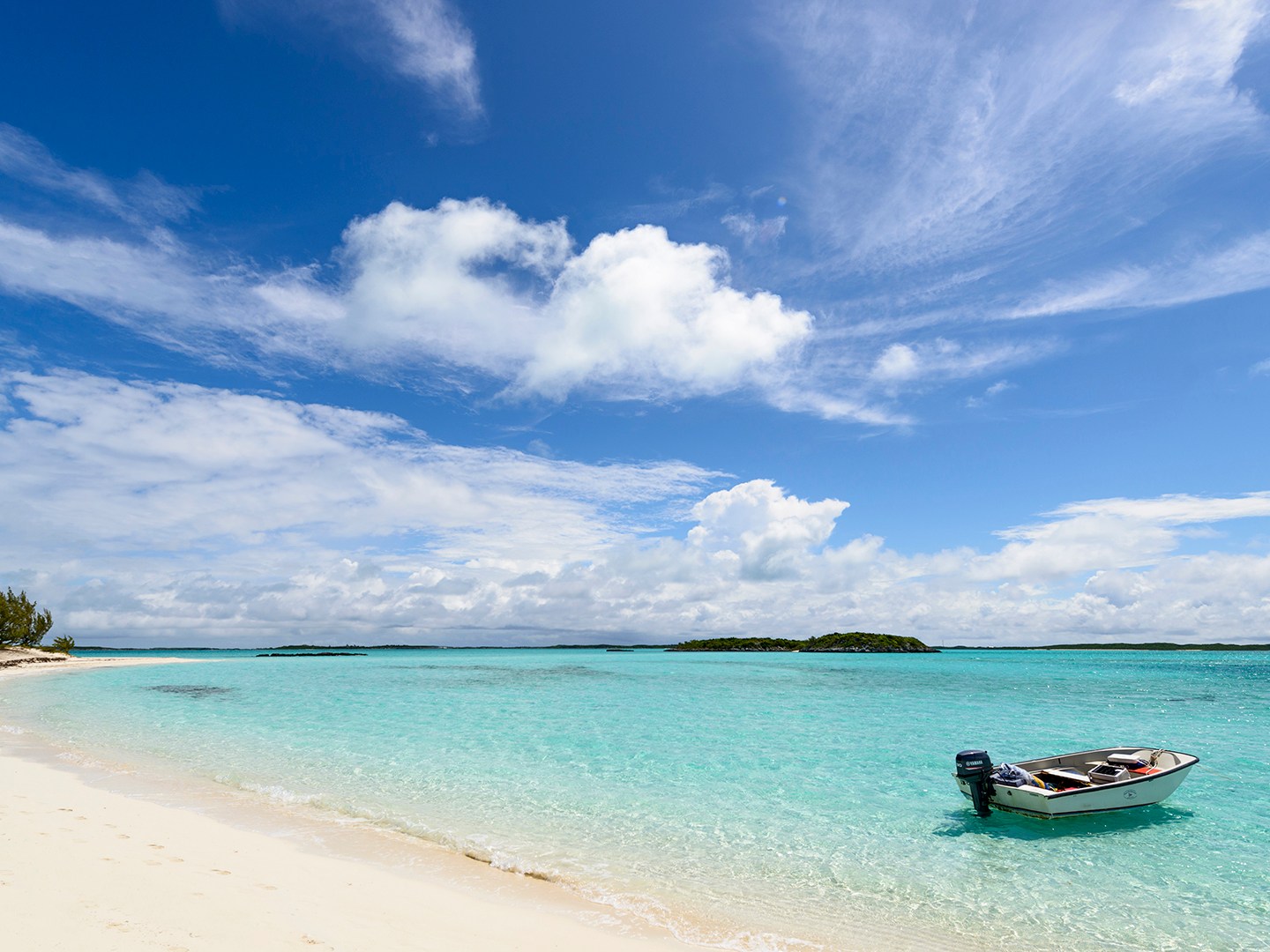 Boat on turquoise water beside sandy beach under a blue sky with clouds.